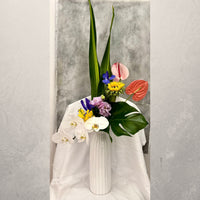 With Love & Grace contemporary orchid arrangement featuring white Phalaenopsis orchids, pink anthurium and lush tropical foliage in a modern ceramic vase.