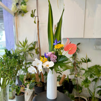 With Love & Grace contemporary orchid arrangement featuring white Phalaenopsis orchids, pink anthurium and lush tropical foliage in a modern ceramic vase.