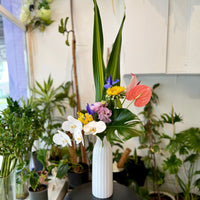 With Love & Grace contemporary orchid arrangement featuring white Phalaenopsis orchids, pink anthurium and lush tropical foliage in a modern ceramic vase.
